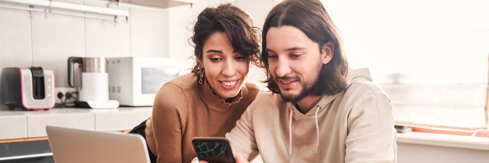 Couple looking at phone with computer open